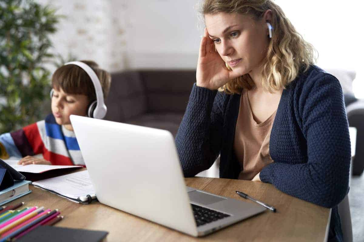 Frustrated mother working from home with young son sitting next to her.