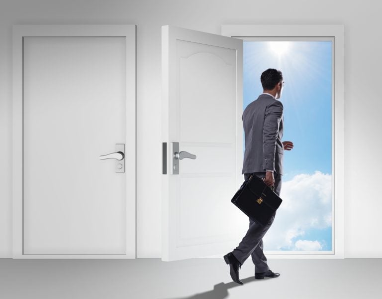 A man in a suit, holding a briefcase, walks through an open door into a bright, sunny sky. Another closed door is visible beside him.