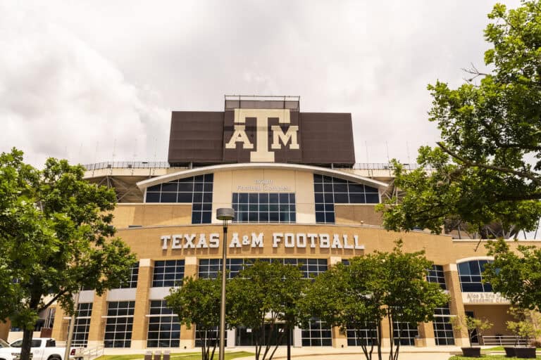 Exterior view of the Texas A&M Football stadium, featuring a large "ATM" logo and surrounded by trees under a cloudy sky.