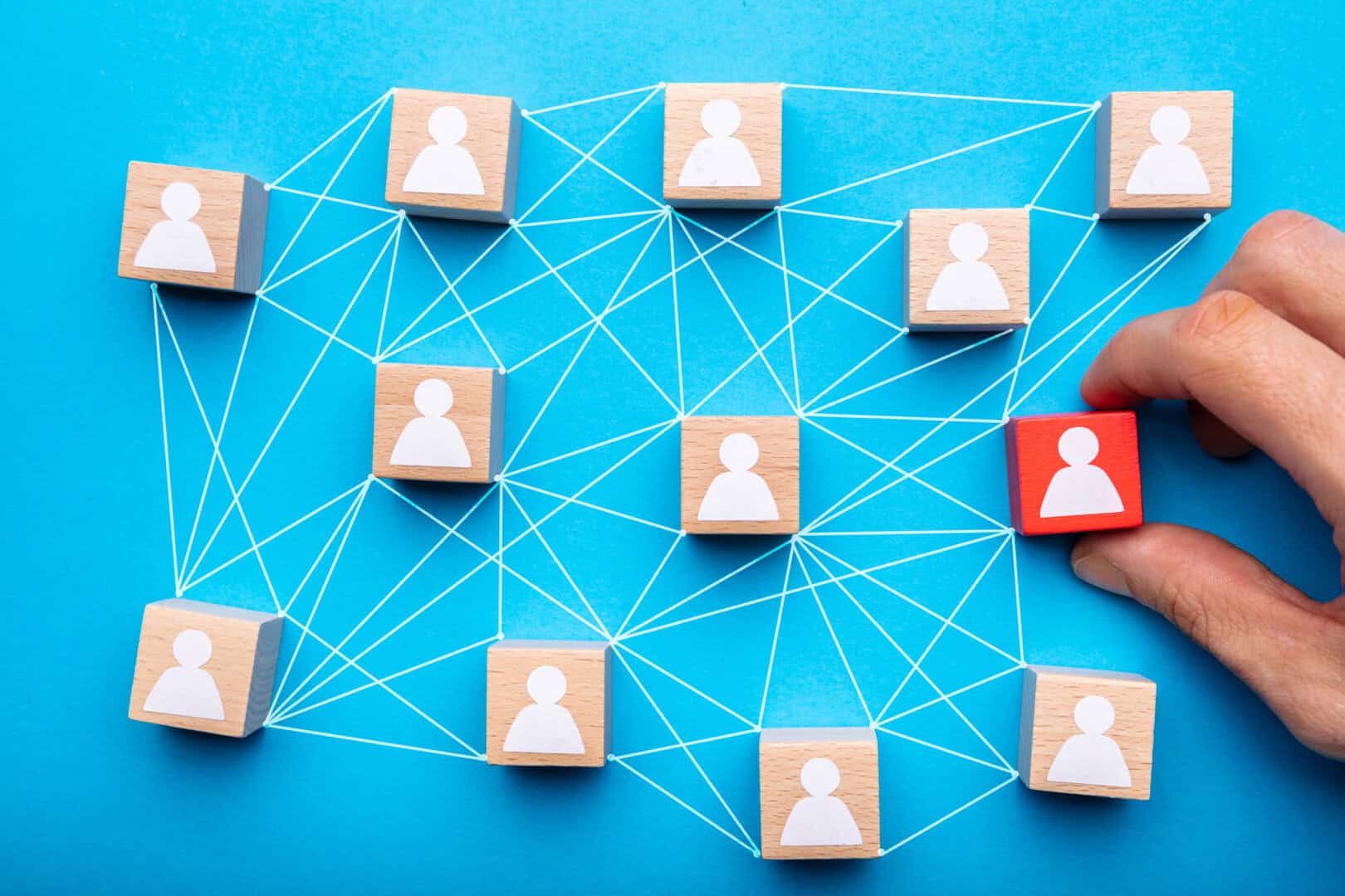 A hand moves a red block with a person icon among wooden blocks connected by white lines on a blue background, representing a network or organizational structure.