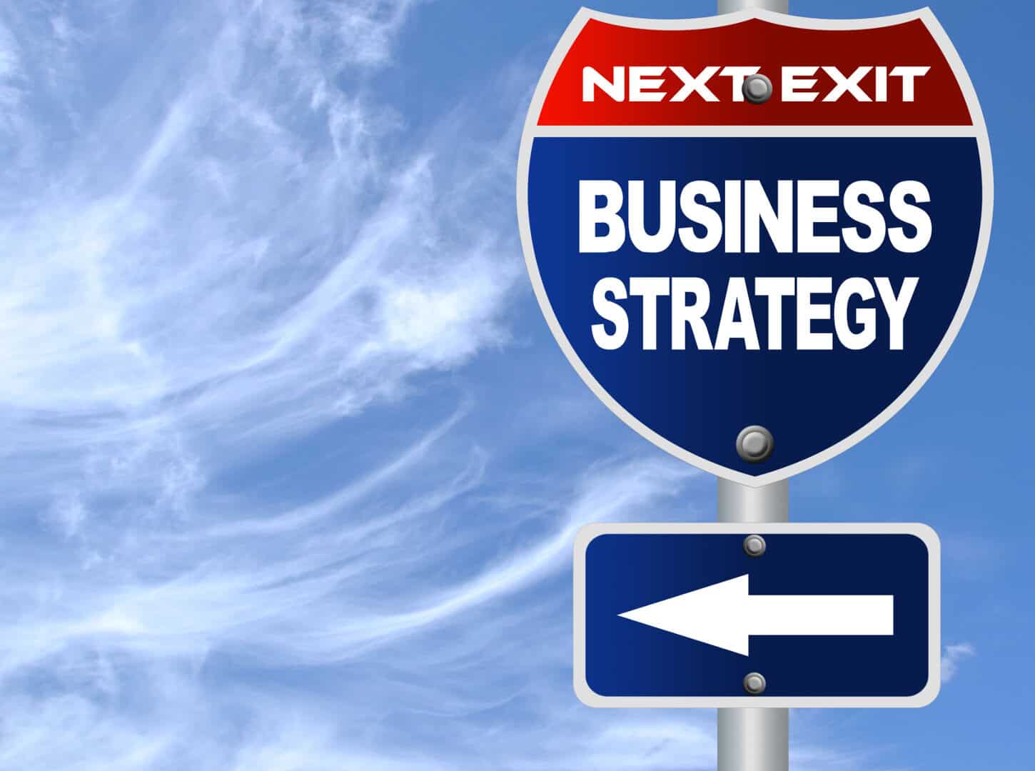 Highway sign reads “Next Exit Business Strategy,” with an arrow pointing left, set against a blue sky with wispy clouds.